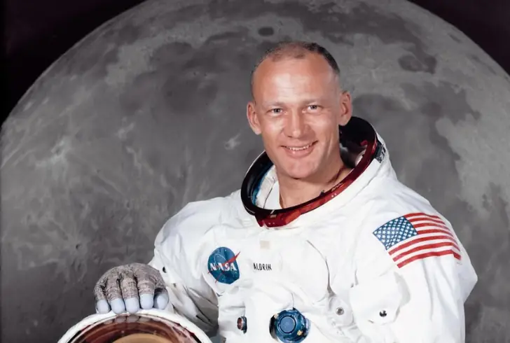 A portrait of Buzz Aldrin in his astronaut suit with the moon in the background